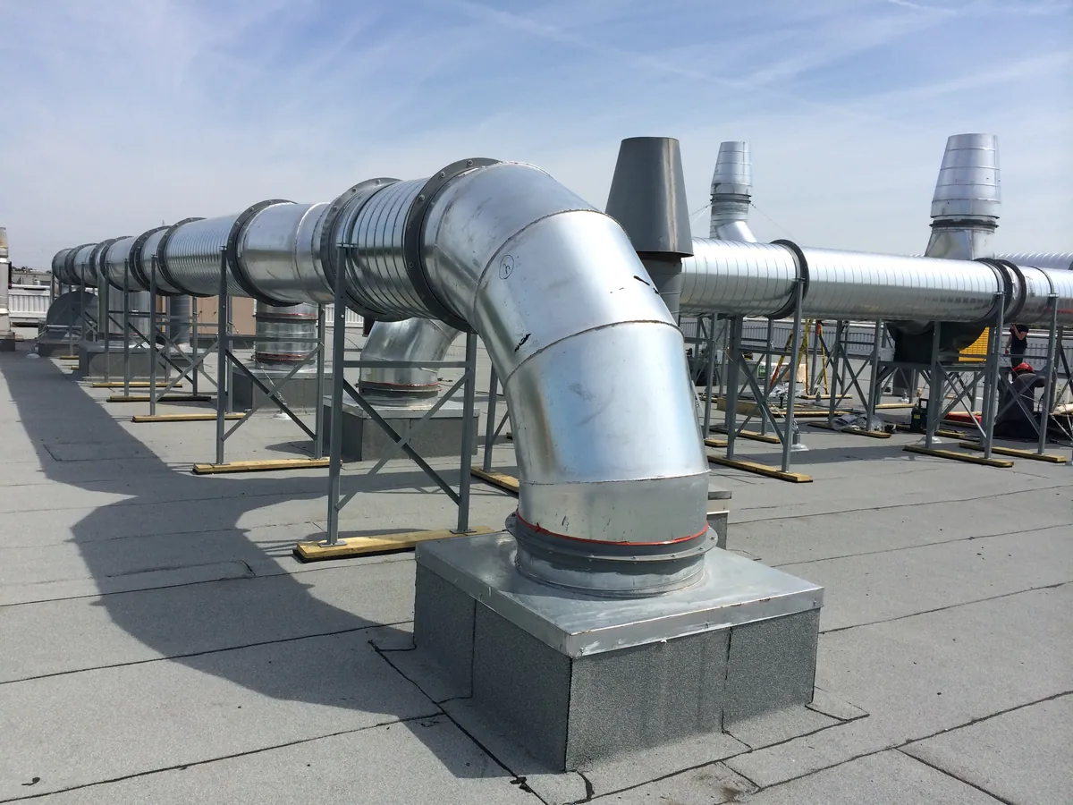 Réseau de gaines d'extraction en acier galvanisé sur un toit-terrasse, sous un ciel bleu